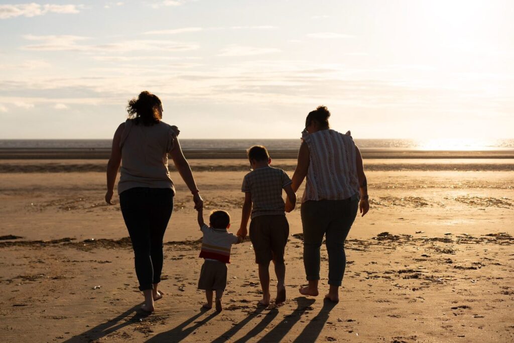 A family of 4 on the beach. They have their backs to the camera and they are all holding hands